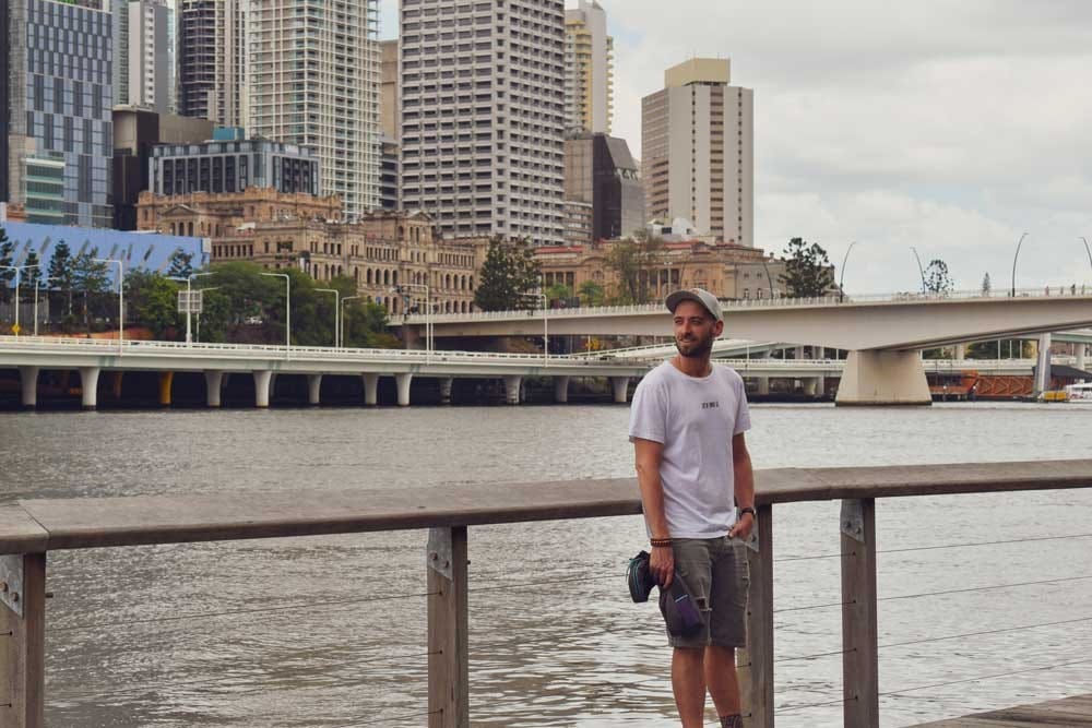 Ciudad de Brisbane chico moreno posando y detrás una ciudad con un rió